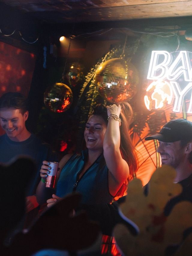Bezoekers lachen voor het neonbord en de discoballen